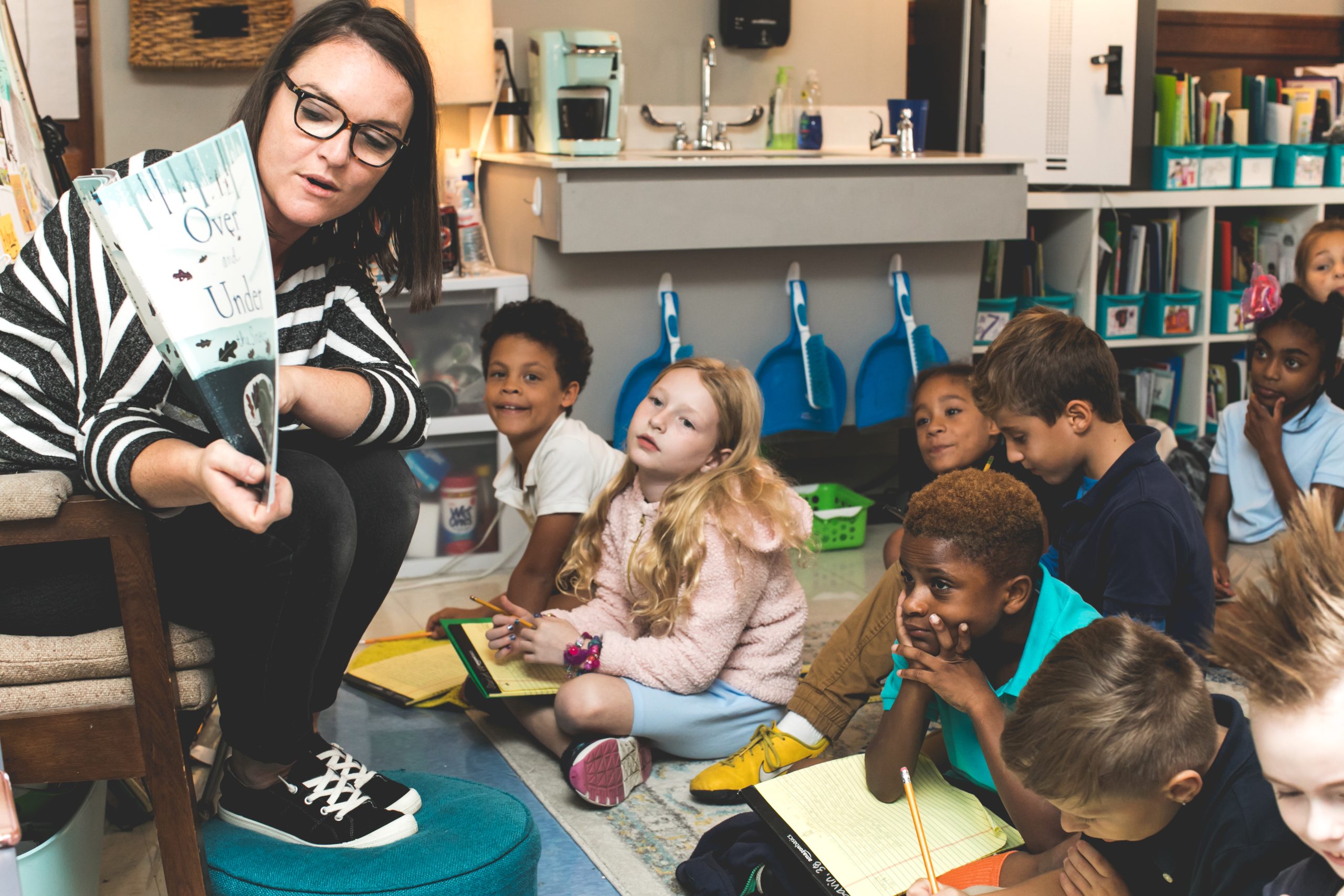 Teacher reading a book to a group of students seated together on the floor in a classroom