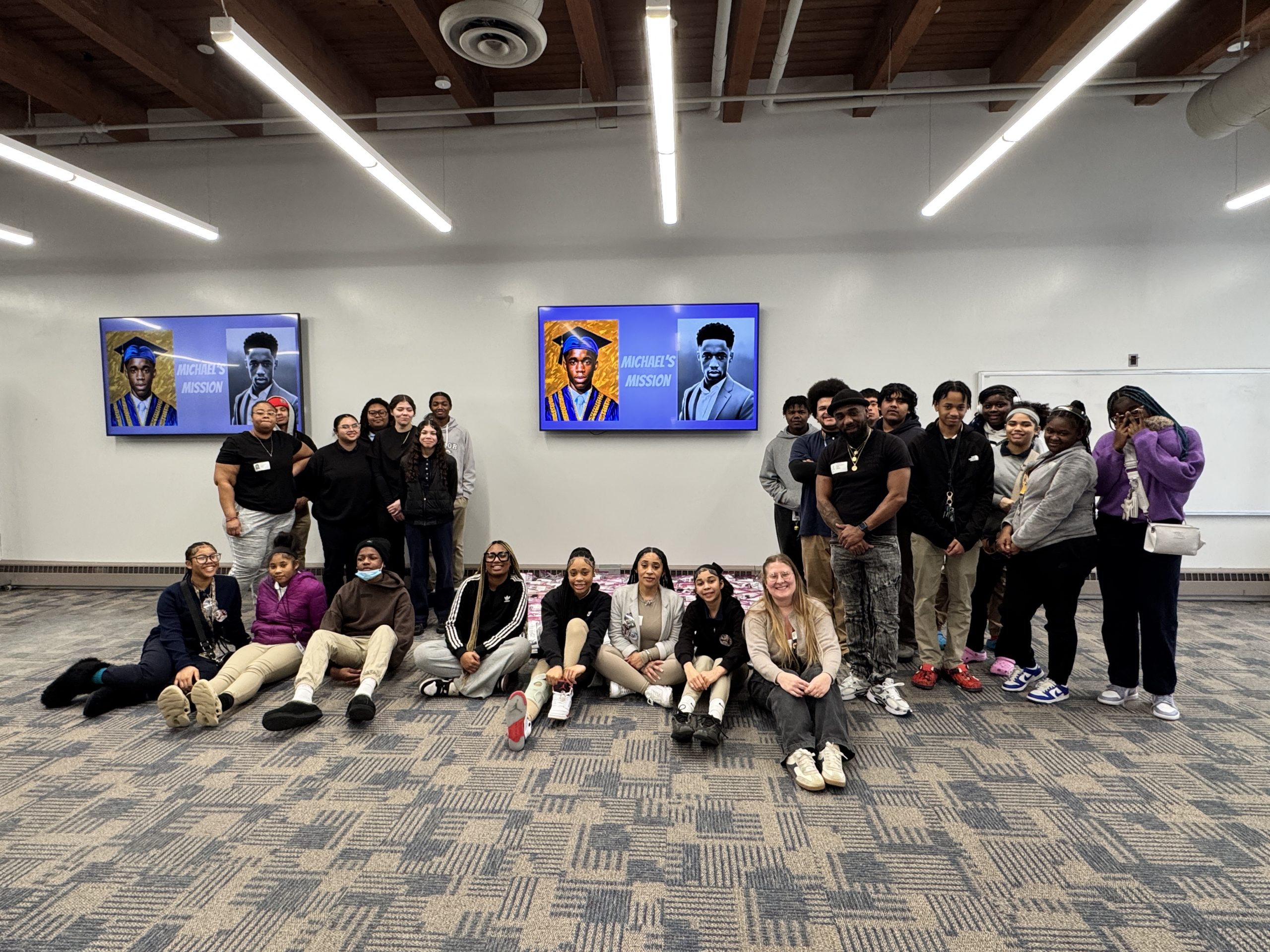 Students and teachers posing against the wall next to a memorial