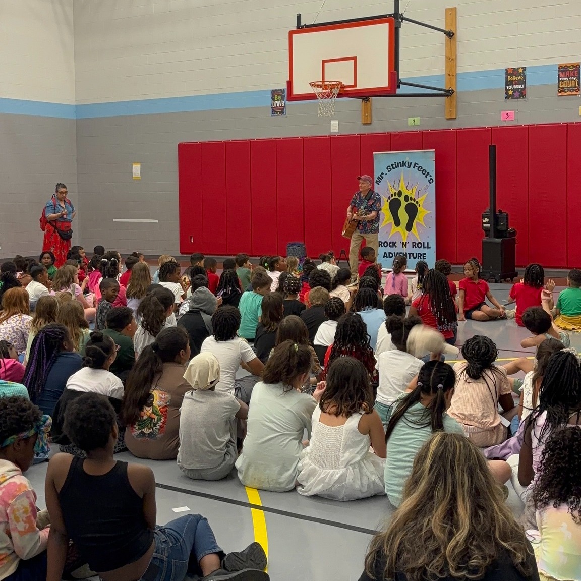 Students sitting in a gym and listening to an artist play music on a guitar