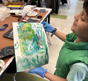 Student proudly displaying their artwork and smiling