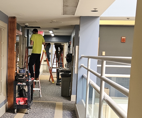 Man using a ladder to fix vents in school hallway