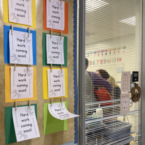Wall displaying paper with 'Hard work coming soon' written on it